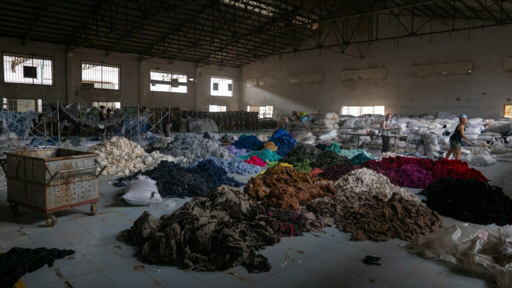 Grote hal vol gesorteerd textielafval toont de impact van fast-fashion op inzamelsystemen.