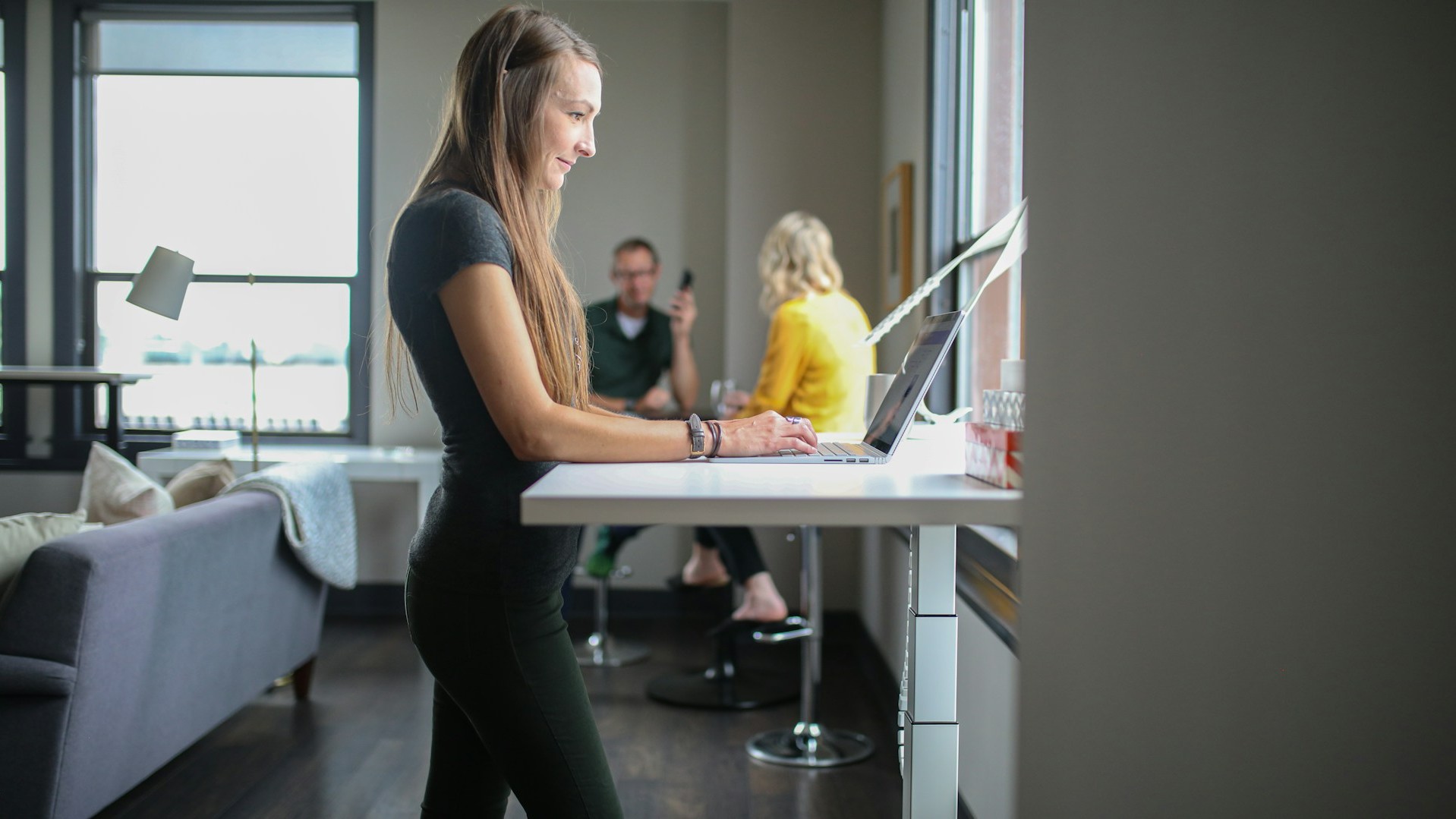 Vrouw werkt staand aan laptop op een ergonomisch verstelbaar bureau in een moderne kantooromgeving