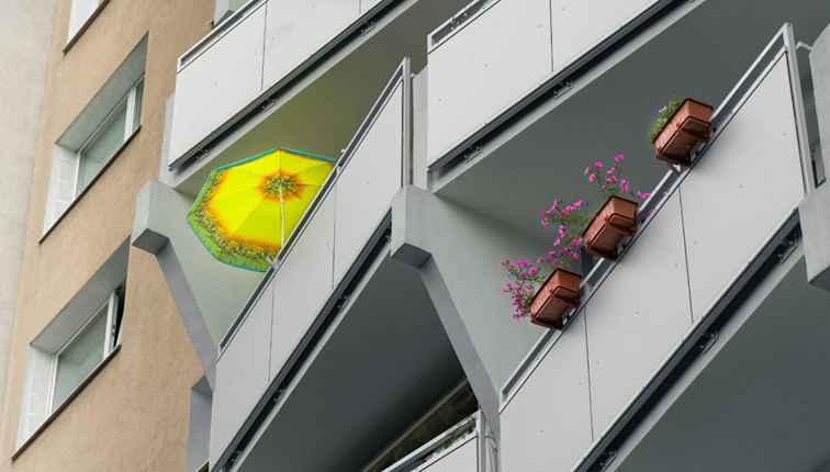 Appartementencomplex met balkonbakken vol bloemen en een opvallende gele parasol