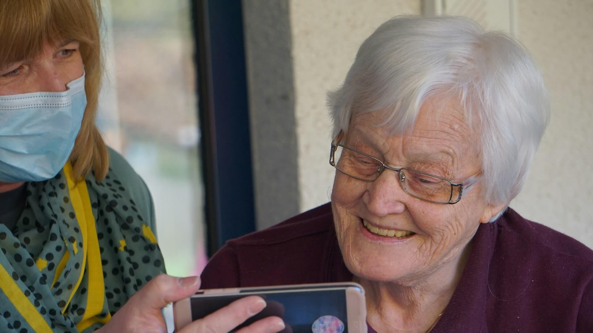 Mantelzorger helpt oudere met smartphone binnen dementiezorg thuis voor communicatie en ondersteuning